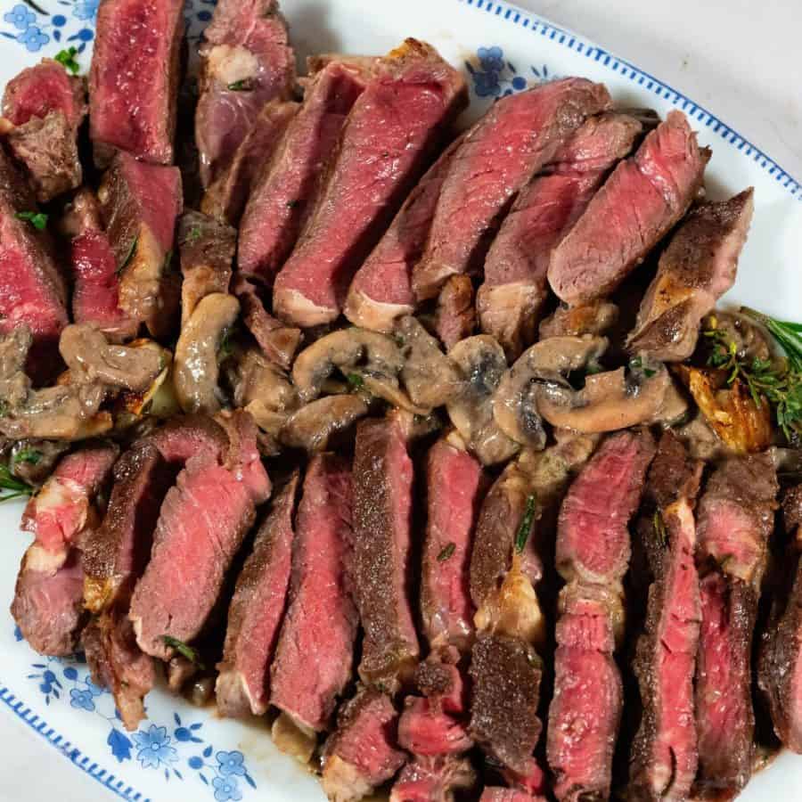 A platter with sliced steak over mushroom sauce.