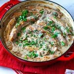 A red dutch oven with sausages and mushrooms.