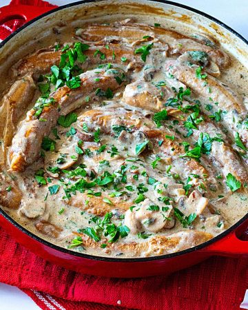 A red dutch oven with sausages and mushrooms.