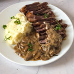 A plate with mashed potatoes red wine steak sauce and steak.