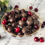 A platter with chocolate dipped cherries on the cake stand.