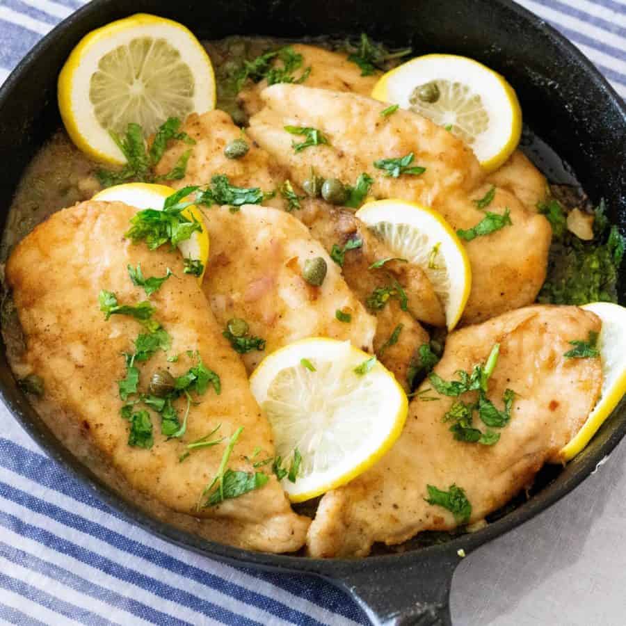 A cast iron pan with chicken in piccata sauce.