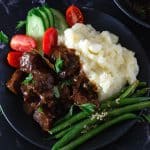 A black bowl with beef tips, mashed potatoes and beans.