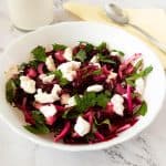 A white bowl with beets and goat cheese.