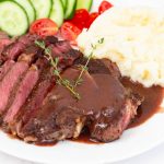 A white plate with red wine steak sauce over med rare steak.
