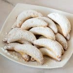 A white plate with cookies dusted in sugar.