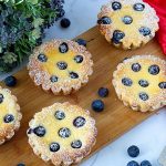 Six mini blueberry cheesecake tarts on the board.