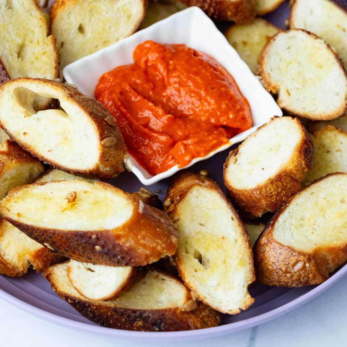A plate with crostini and roasted red pepper spread.