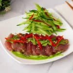 A white plate with fresh tuna and green cilantro sauce.