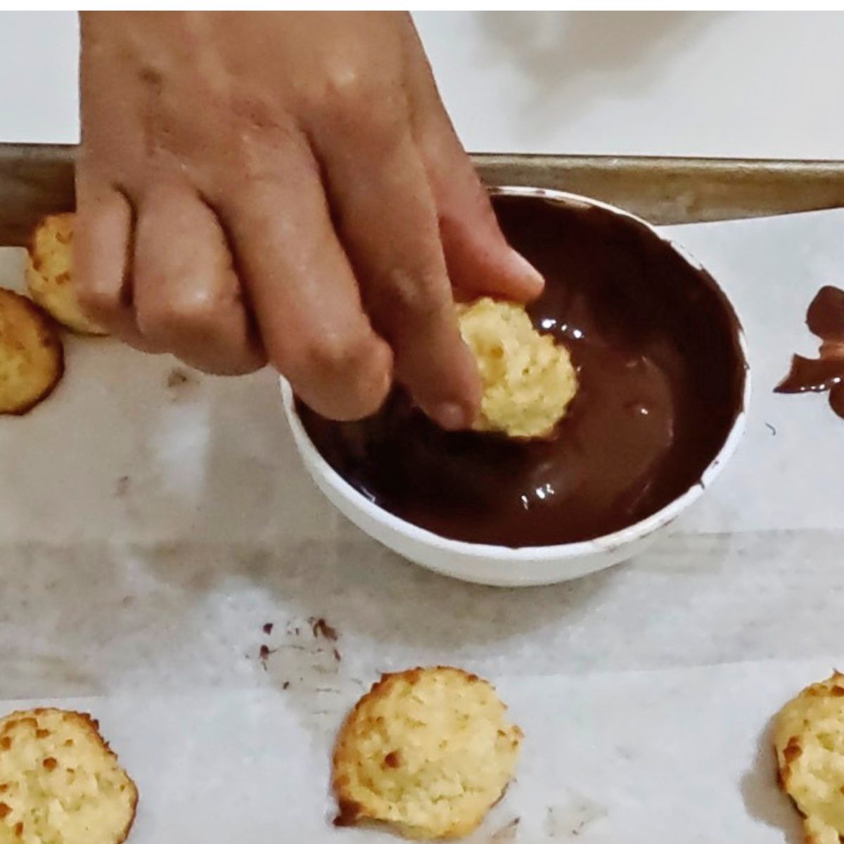 Dipping coconut macaroon in chocolate.