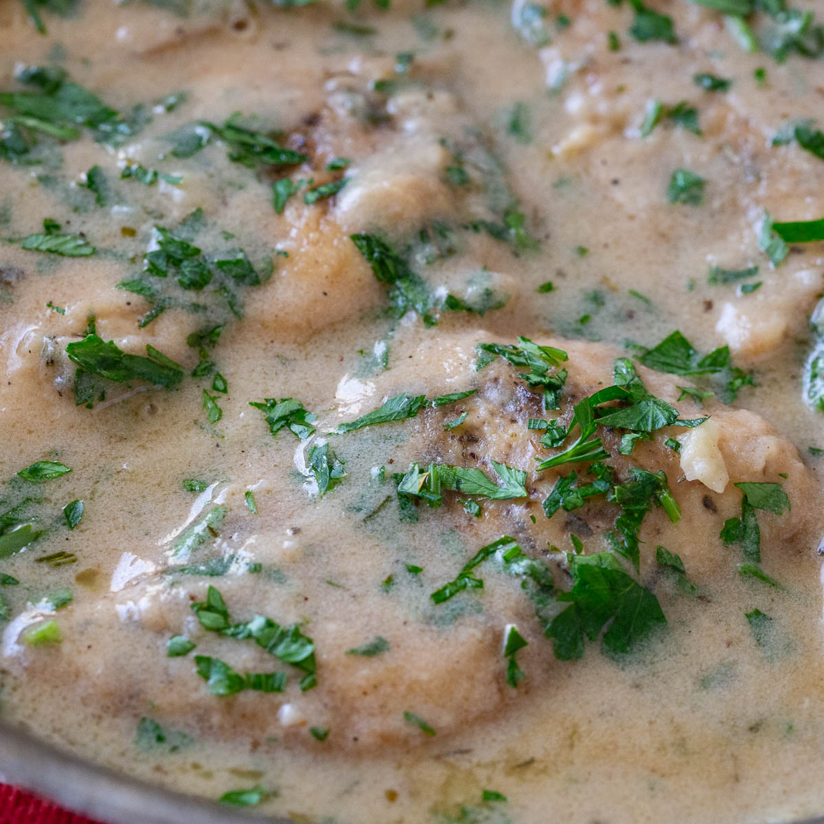 A frying pan with chicken cutlet in sauce.