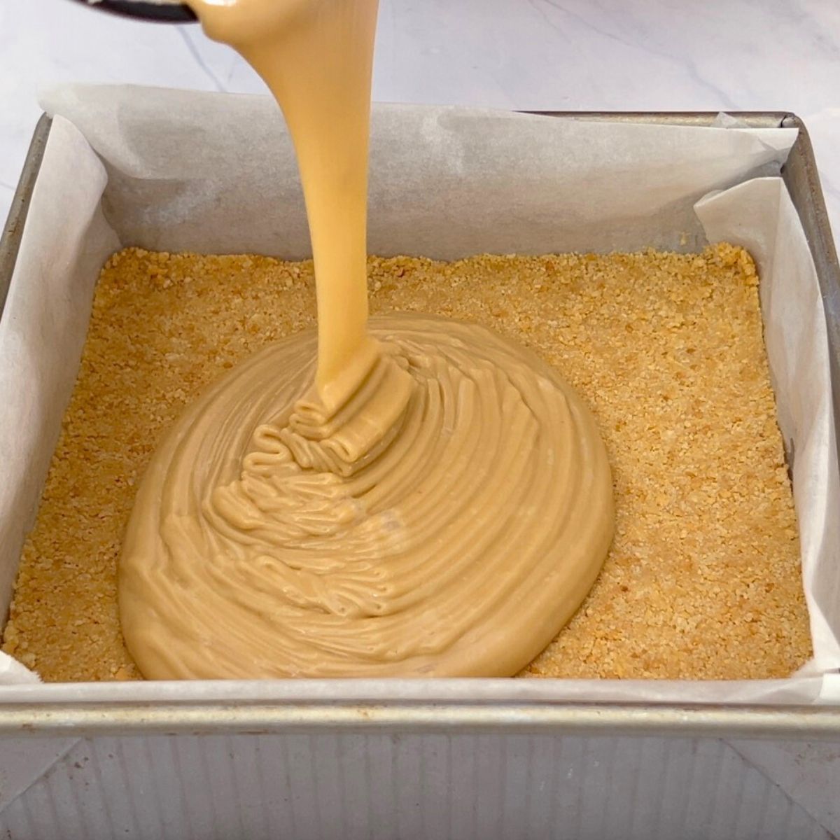 Pouring coffee fudge over graham cracker crust,