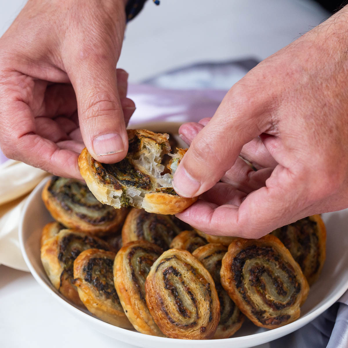 Hands cracking the pinwheel appetizers over a plate.