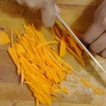 A wooden cutting board with shredded carrots.