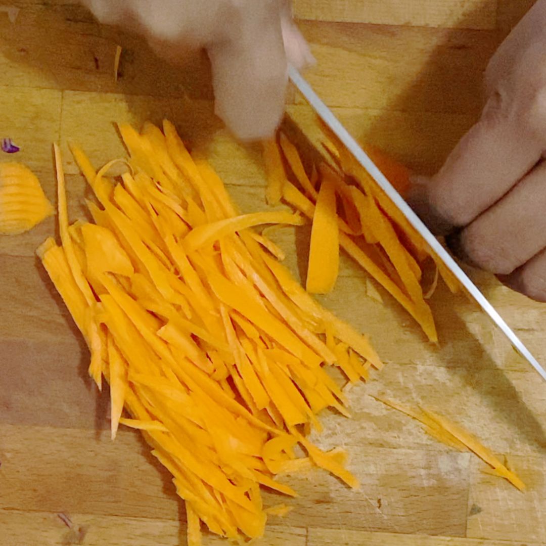A wooden cutting board with shredded carrots.