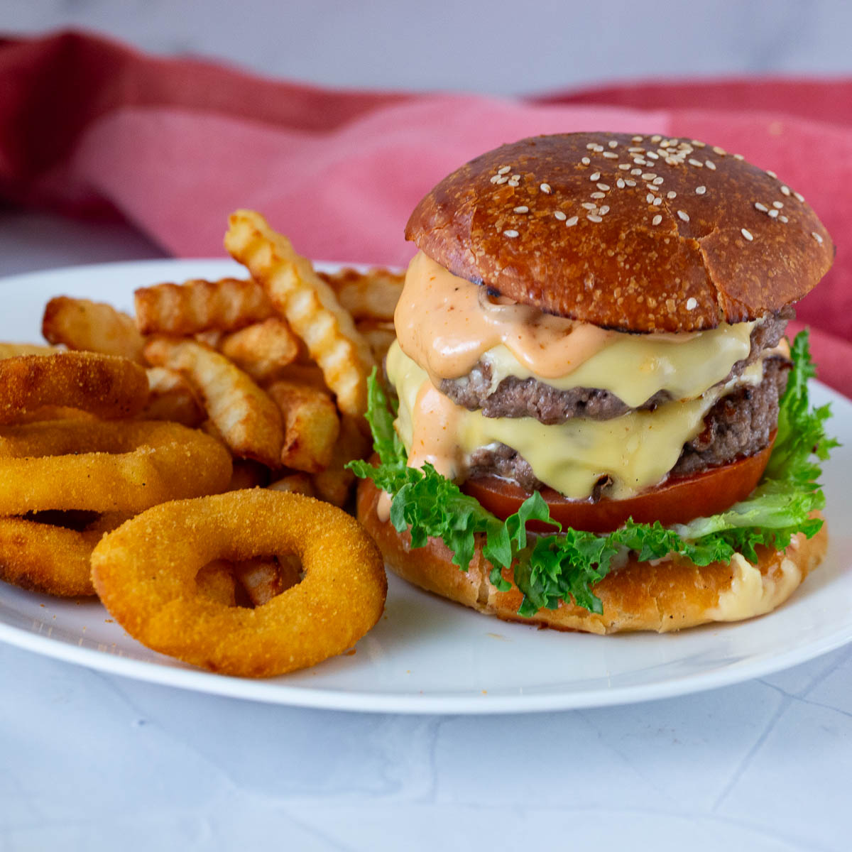 A double patty burger with fries and onion rings on the plate.