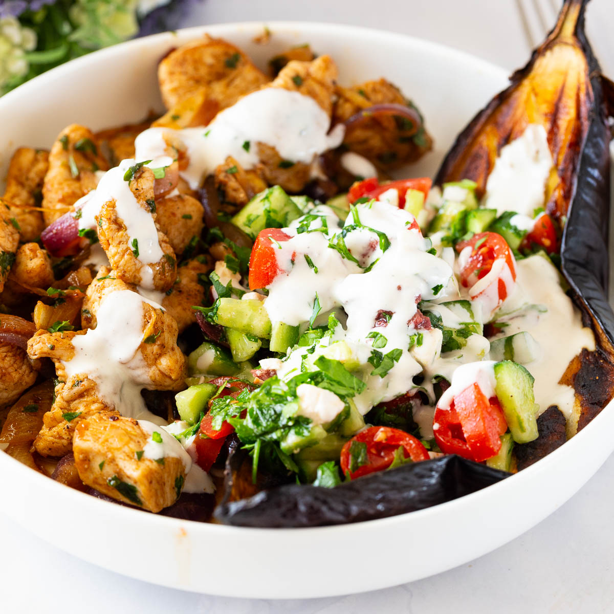 A white plate with chicken and baked eggplant and salad.