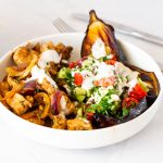 A white plate with chicken and baked eggplant dinner.