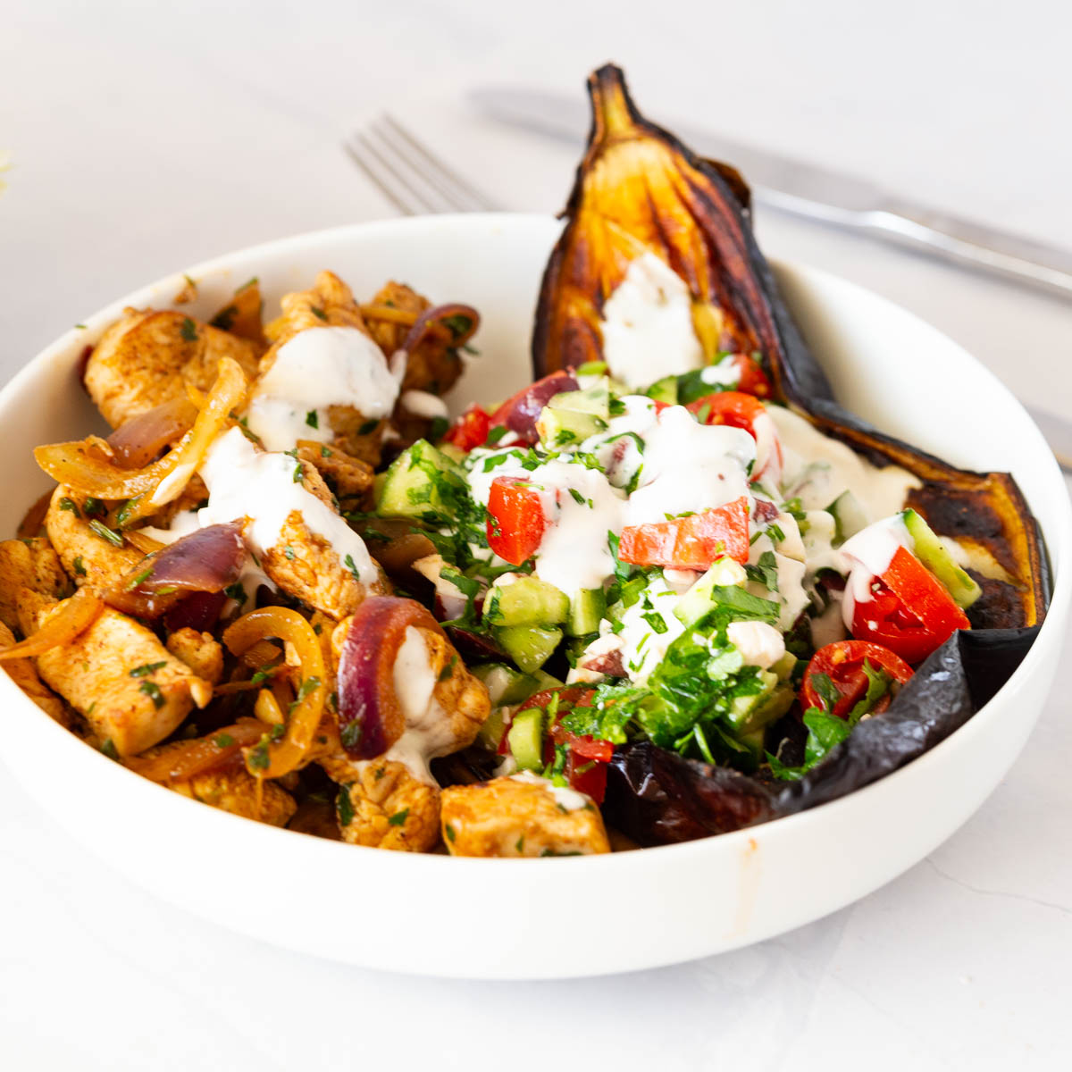 A white plate with chicken and baked eggplant dinner.