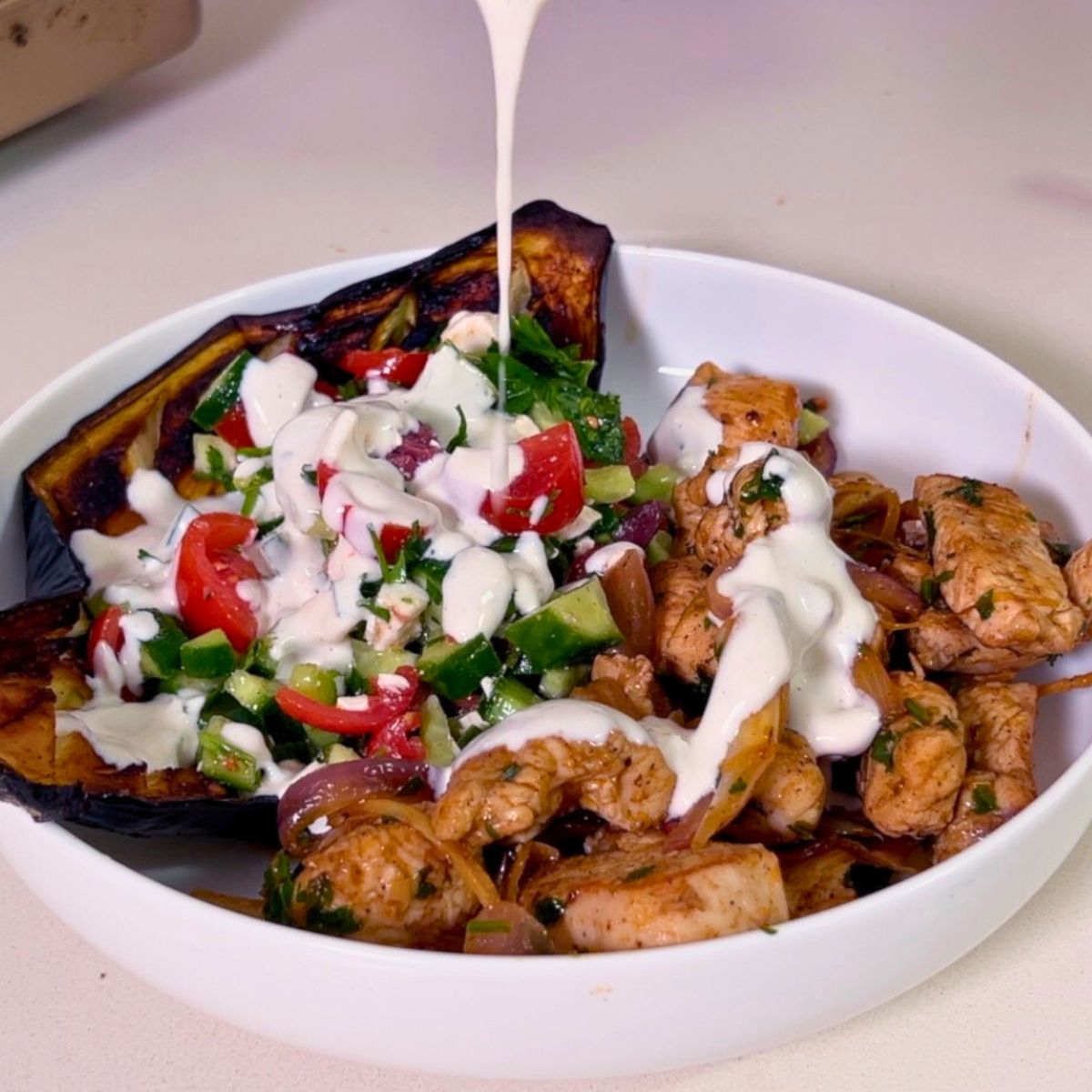 A plate with chicken eggplant salad and drizzling tahini.