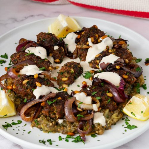 A platter with roast eggplant and kebabs.