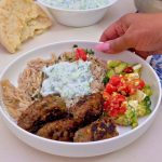 A white plate with Greek kofta kebabs with rice and tzatziki sauce.