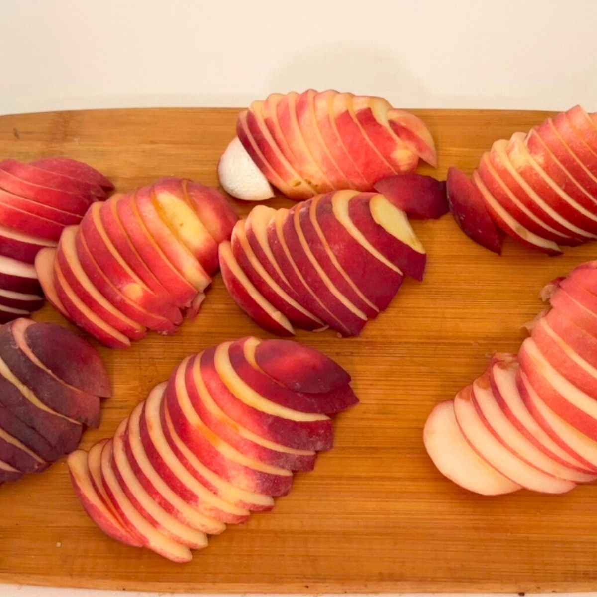 Fresh peaches sliced on a wooden cutting board.
