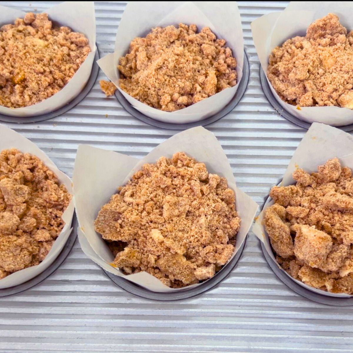 A muffin pan with pumpkin batter cream cheese and crumble.