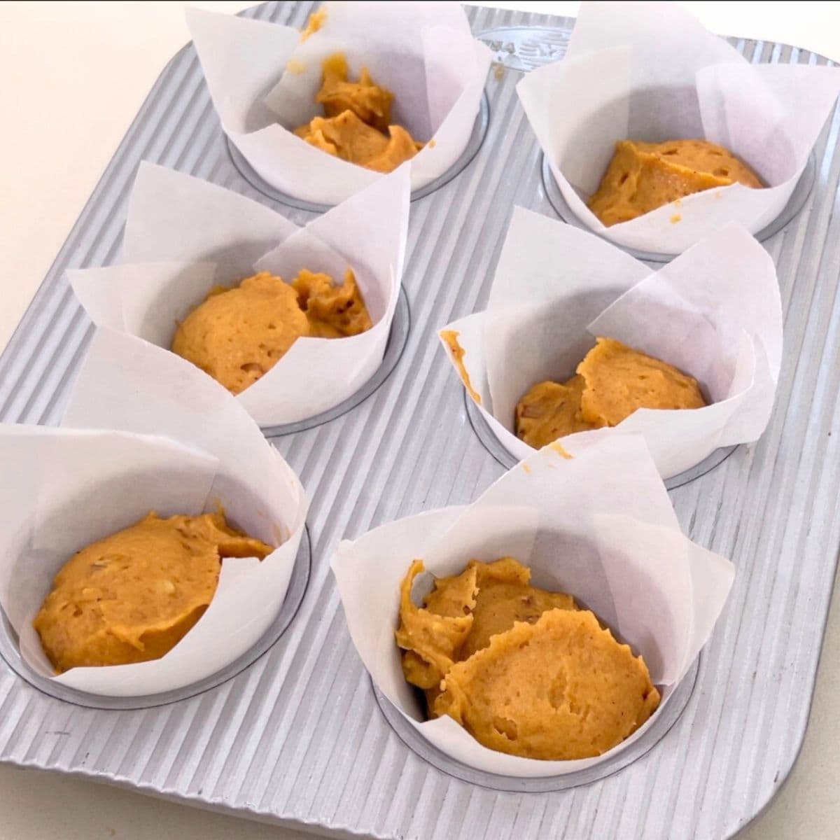 A muffin pan with pumpkin muffins batter.