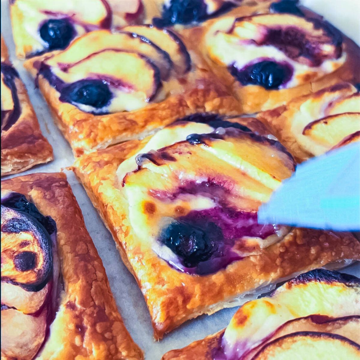 Golden blueberry peach puff pastry tarts cooling on a baking sheet.