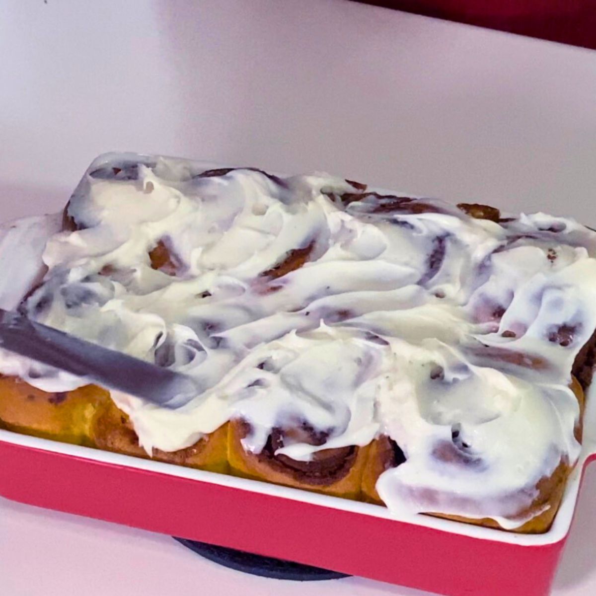 A freshly baked dish with frosting cinnamon rolls.