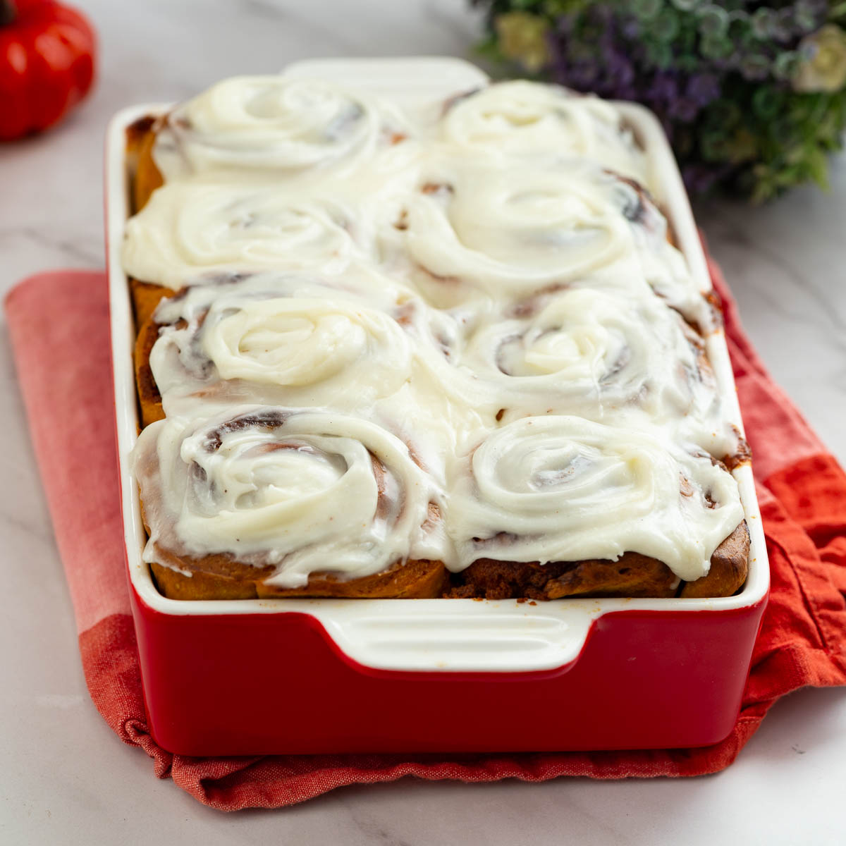 A baking dish with pumpkin cinnamon rolls and cream cheese top.