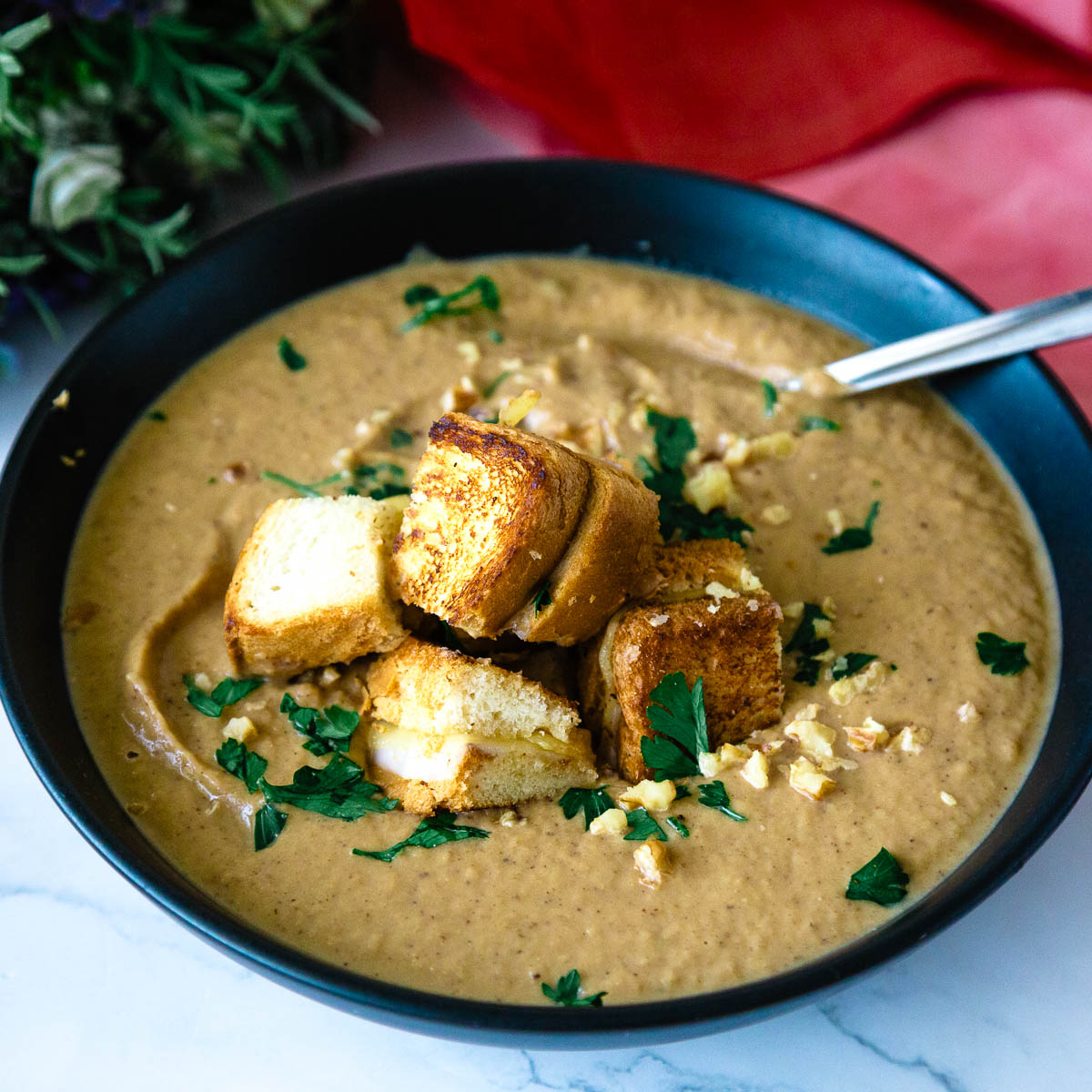 A black bowl with roasted cauliflower soup, croutons, and garnish.