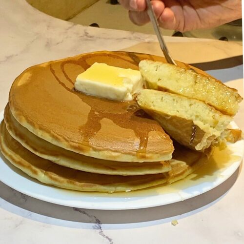 Two fluffy pancakes on a white plate with butter and maple.