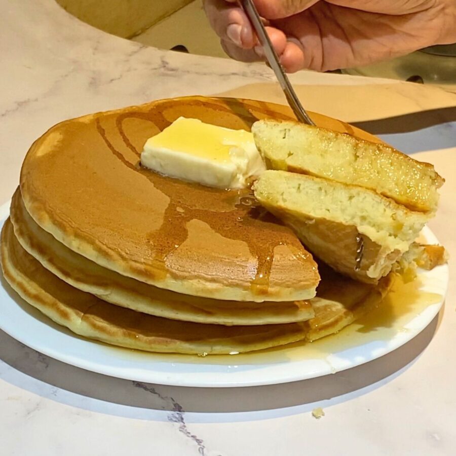 Three fluffy pancakes cut into a wedge on a white plate.