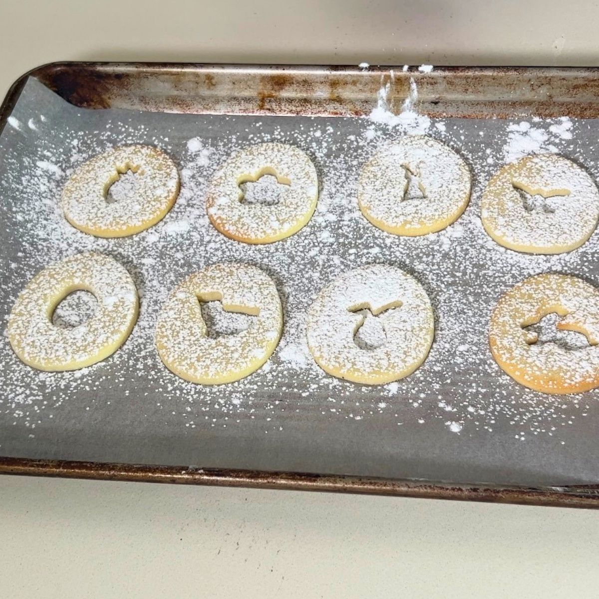 Tops of sandwich cookies dusted with powdered sugar on baking tray.