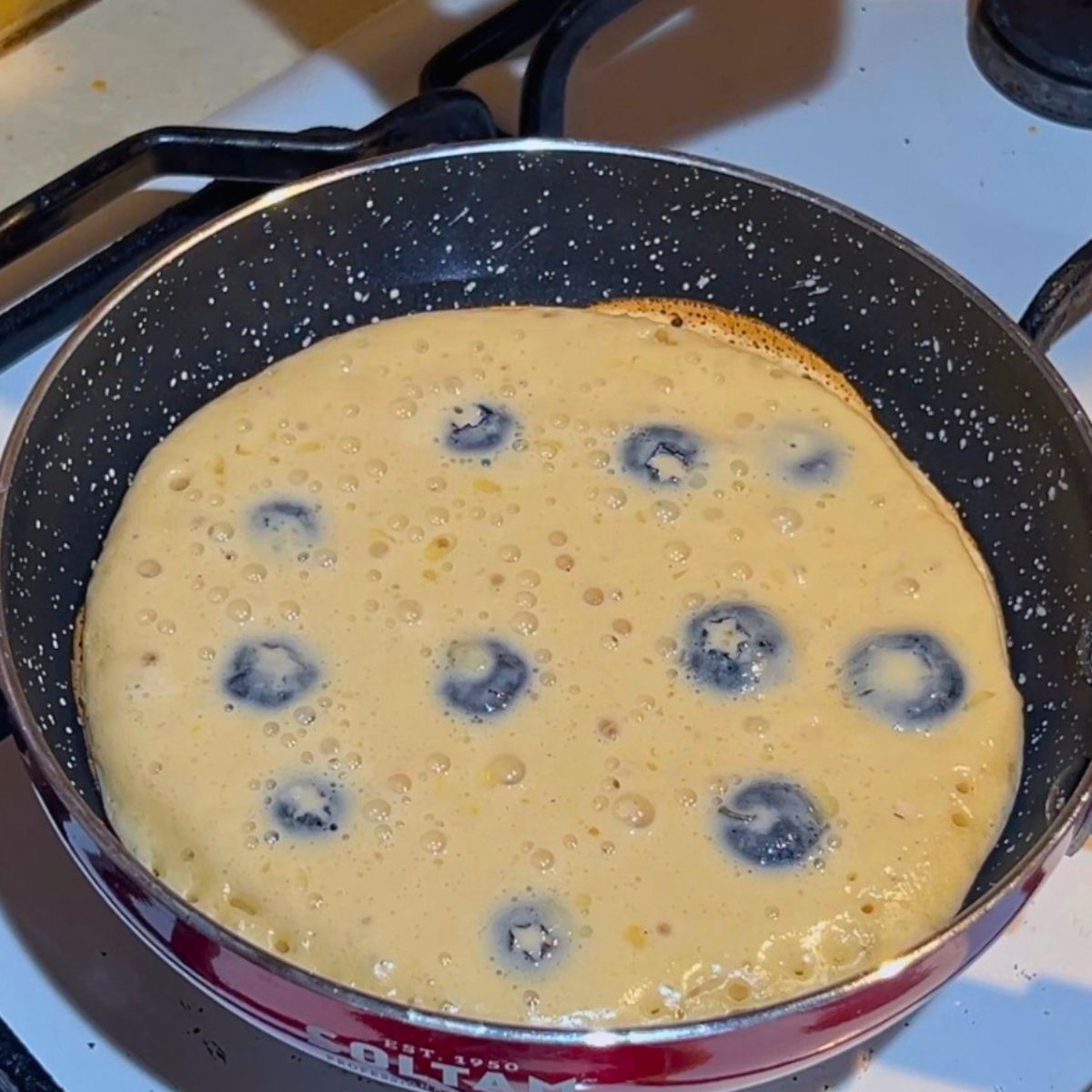 Frying pan with fresh blueberries pancake batter.