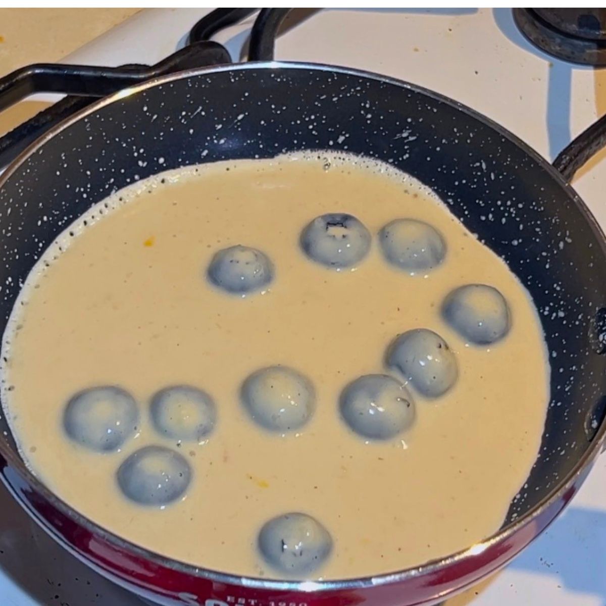 A frying pan with fresh blueberries pancake batter.
