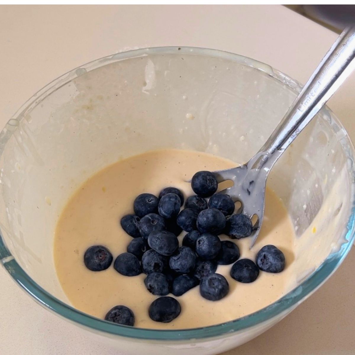 A glass bowl with pancake batter and fresh blueberries.