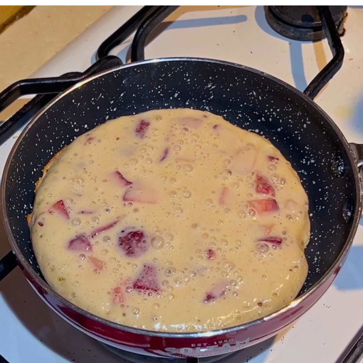 A frying pan with strawberry pancake half cooked.