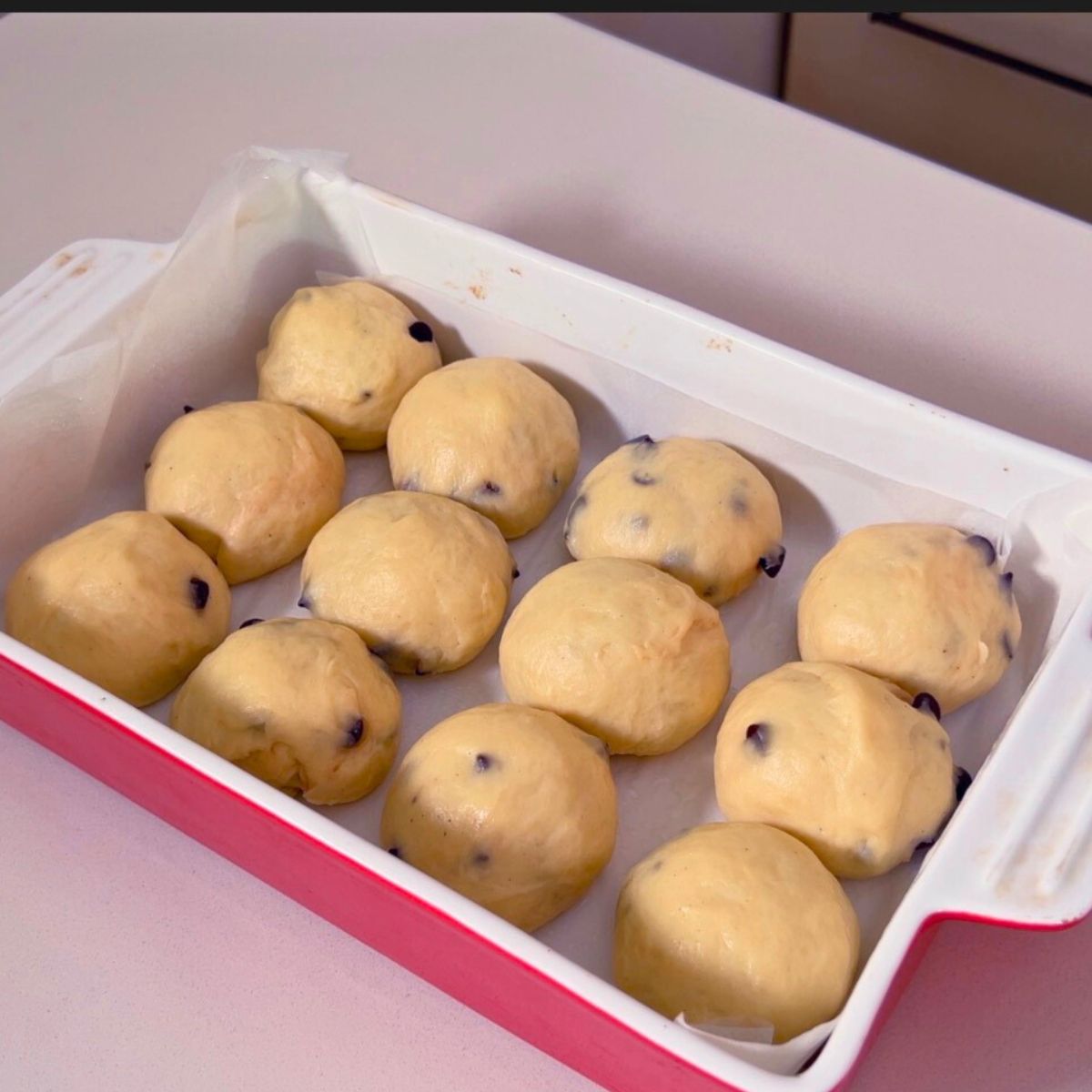 Proofed hot cross buns in a baking pan.