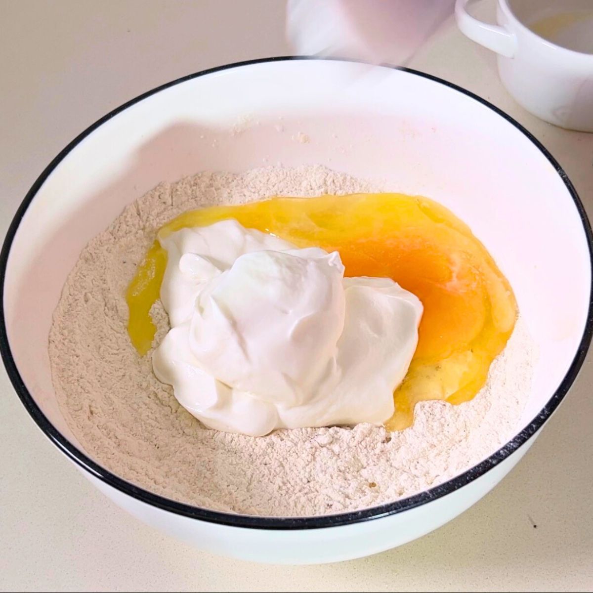 Preparing Greek Yogurt dough in a white bowl.