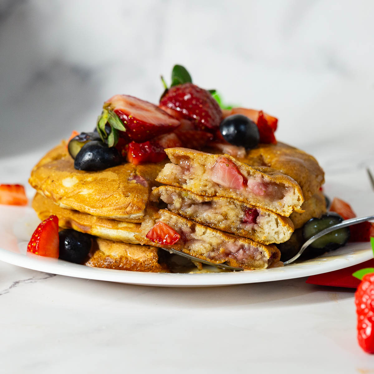 A cut-up stack of strawberry pancakes on the white plate.