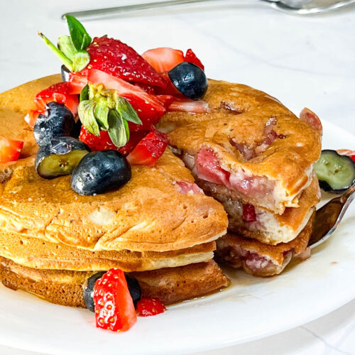Fresh strawberry pancakes cut into with a knife.