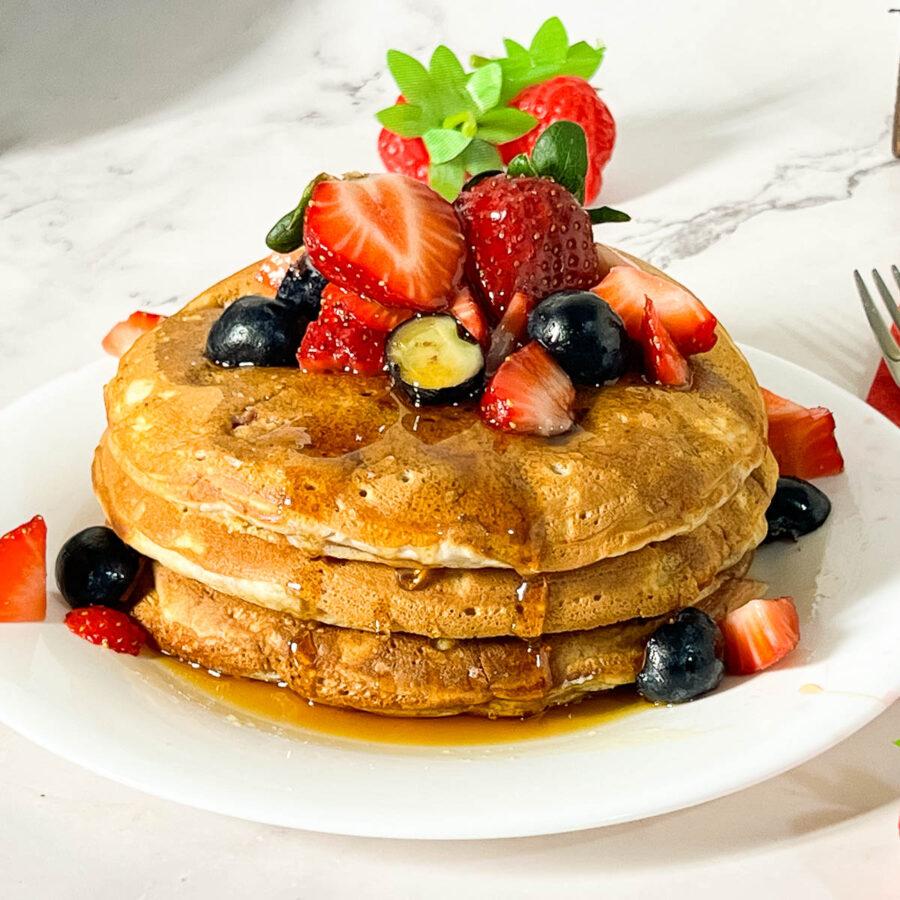 A stack of strawberry pancakes on the table.