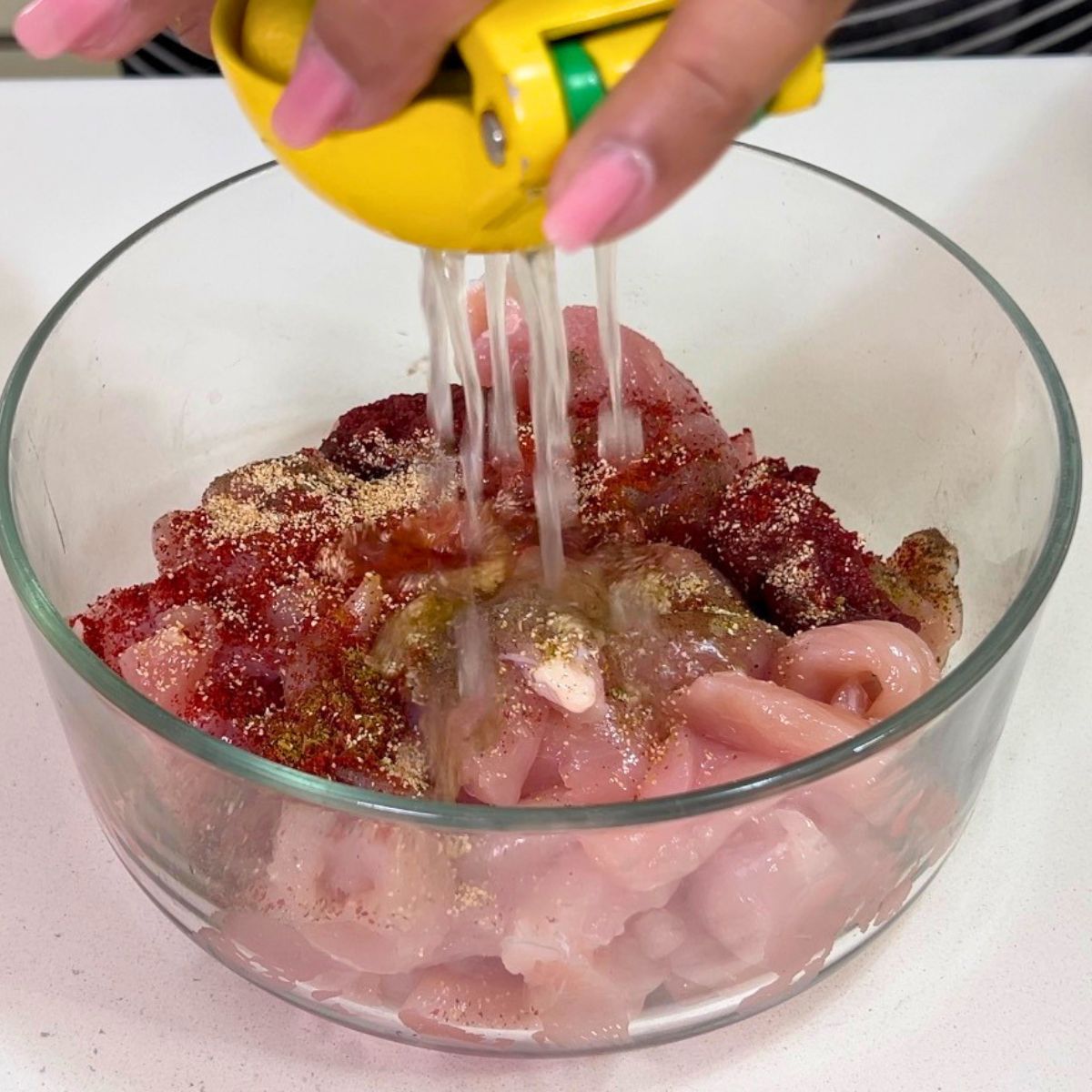 A glass bowl with chicken in taco seasoning.