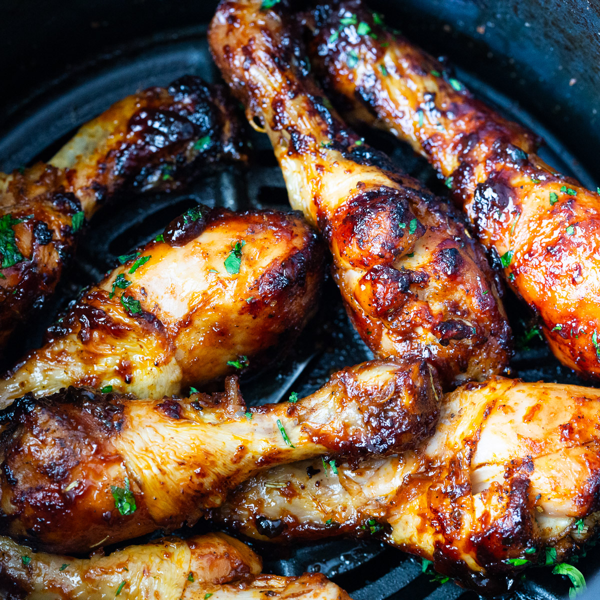 An air fryer basket with baked chicken legs.