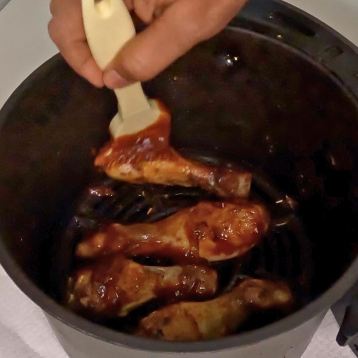 A air fryer basket with BBQ chicken legs and BBQ sauce.
