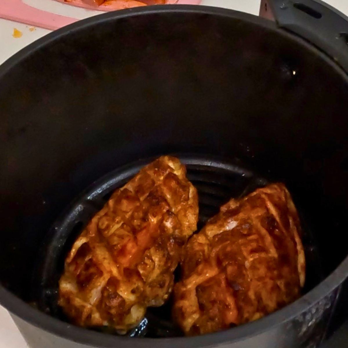 Air fryer basket with chicken breast.