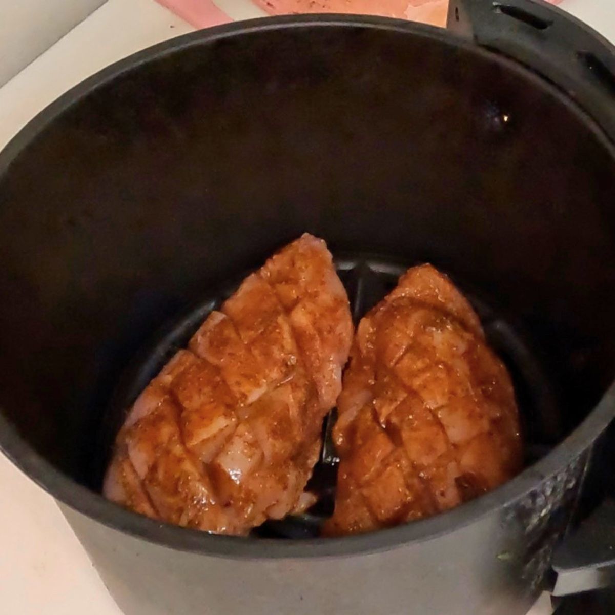 Chicken in air fryer basket for baking.